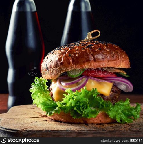 delicious burger with fried beef cutlet, tomato, lettuce and onions, crispy white wheat flour bun with sesame seeds. Fast food on a wooden board, behind a bottle with a drink