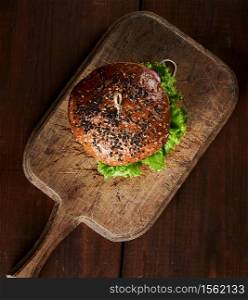 delicious burger with sesame bun on vintage brown cutting board, top view, wooden table
