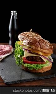 delicious burgers with fried beef cutlet and onions, tomato and crispy white wheat flour bun with sesame seeds. Fast food on a wooden board, behind a bottle with a drink