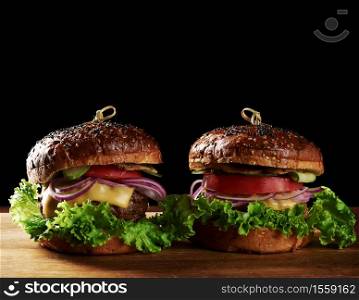 delicious burgers with fried beef cutlet, tomato, lettuce and onions, crispy white wheat flour bun with sesame seeds. Fast food on a wooden board