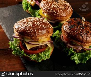 delicious burgers with fried beef cutlet, tomato, lettuce and onions, crispy white wheat flour bun with sesame seeds. Fast food on a wooden board