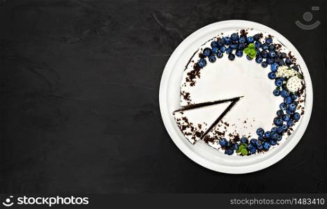 Delicious cake layout with copy space. Homemade bird cherry cake with sour cream, decorated with blueberries and mint leaves on a plate. Siberian traditional cake, dark background. Homemade bird cherry cake with sour cream, decorated with blueberries and mint leaves on a plate. dark background