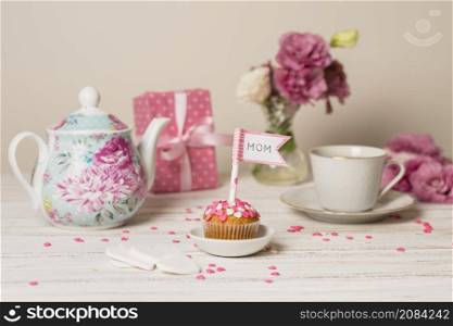 delicious cake with decorative flag with mom title near teapot flowers cup