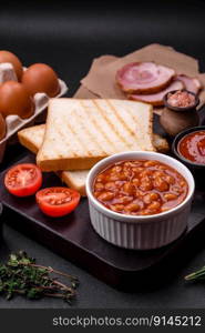 Delicious canned beans in a tomato in a white ceramic bowl on a dark concrete background