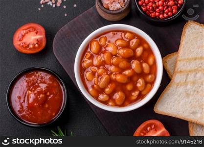 Delicious canned beans in a tomato in a white ceramic bowl on a dark concrete background