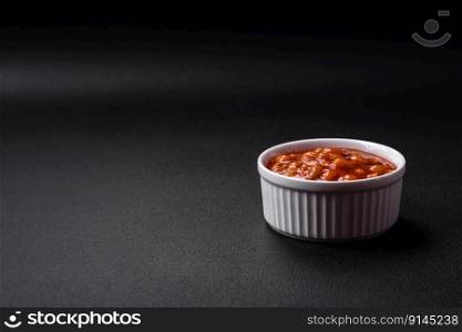 Delicious canned beans in a tomato in a white ceramic bowl on a dark concrete background
