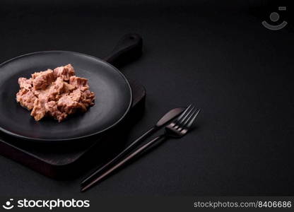 Delicious canned tuna meat on a black ceramic plate on a dark concrete background. Healthy food preparation