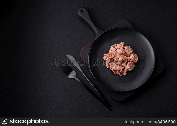 Delicious canned tuna meat on a black ceramic plate on a dark concrete background. Healthy food preparation