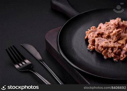 Delicious canned tuna meat on a black ceramic plate on a dark concrete background. Healthy food preparation