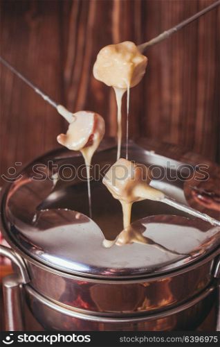 Delicious Cheese Fondue on a fork on a wooden stand. The cheese fondue