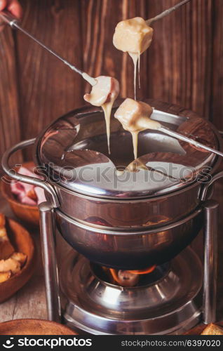 Delicious Cheese Fondue on a fork on a wooden stand. The cheese fondue