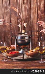 Delicious Cheese Fondue on a fork on a wooden stand. The cheese fondue