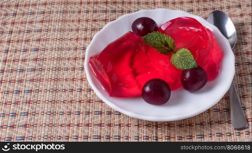 Delicious cherry jelly and ripe cherries with leaves on old blue table.. Jelly in the white plate with ripe cherries