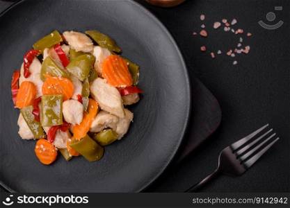Delicious chicken slices and steamed vegetables carrots, broccoli, asparagus beans and peppers on a dark concrete background