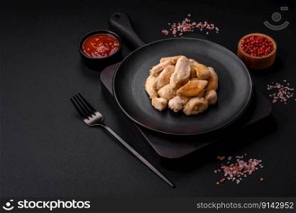 Delicious chicken slices baked with spices and herbs on a round ceramic plate on a dark concrete background