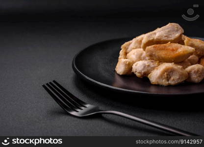 Delicious chicken slices baked with spices and herbs on a round ceramic plate on a dark concrete background