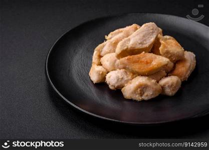 Delicious chicken slices baked with spices and herbs on a round ceramic plate on a dark concrete background