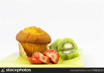 Delicious corn muffin with slices of kiwi and strawberry. Healthy, tasty fruit and baked food on green plate.