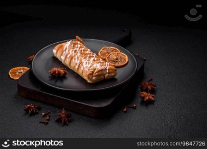 Delicious crispy braided bun with raisins inside and white icing outside on a dark concrete background
