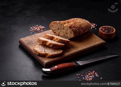 
Delicious crispy bread with cereals cut into slices on a wooden cutting board on a dark concrete background