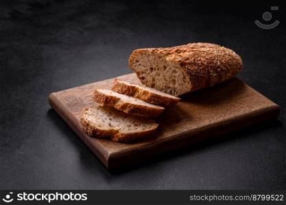 
Delicious crispy bread with cereals cut into slices on a wooden cutting board on a dark concrete background