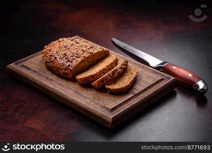 Delicious crispy bread with cereals on a wooden cutting board on a dark concrete background
