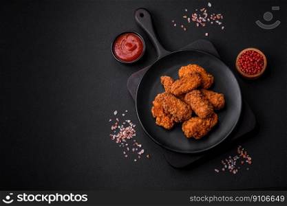Delicious crispy breaded chicken wings grilled with spices and herbs on a dark concrete background