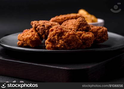 Delicious crispy breaded chicken wings grilled with spices and herbs on a dark concrete background