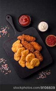 Delicious crispy chicken nuggets with salt and spices on a dark concrete background. Junk food, fast food