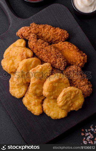 Delicious crispy chicken nuggets with salt and spices on a dark concrete background. Junk food, fast food