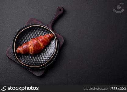 Delicious crispy croissant with chocolate on a black ceramic plate on a dark concrete background