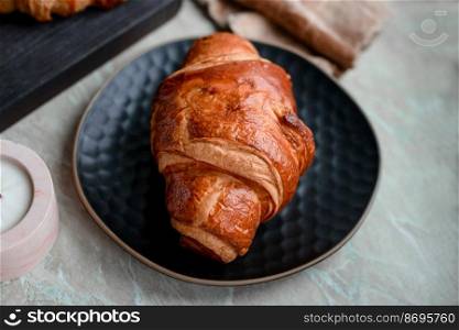 Delicious crispy croissant with chocolate with a cup of invigorating coffee on a light concrete background. Delicious nutritious breakfast