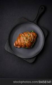 Delicious crispy croissant with salmon, lettuce, cheese and tomatoes on a dark concrete background