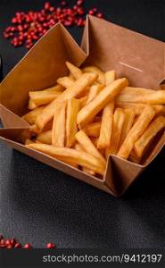 Delicious crispy french fries with salt and spices in a cardboard box on a dark concrete background