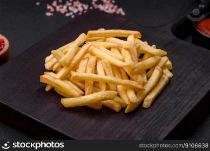 Delicious crispy french fries with salt and spices on a dark concrete background. Unhealthy food, fast food