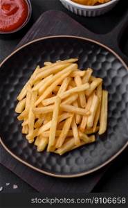 Delicious crispy french fries with salt and spices on a dark concrete background. Unhealthy food, fast food