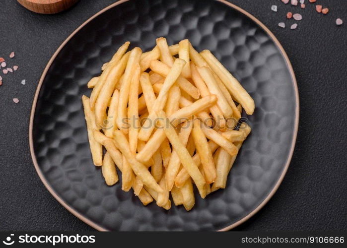 Delicious crispy french fries with salt and spices on a dark concrete background. Unhealthy food, fast food