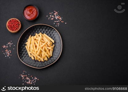 Delicious crispy french fries with salt and spices on a dark concrete background. Unhealthy food, fast food