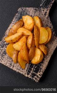 Delicious crispy fried potato wedges with salt, spices and herbs on a dark concrete background