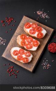Delicious crispy grilled toast with cheese and cherry tomatoes on a dark concrete background