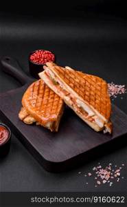 Delicious crispy sandwich with chicken breast, tomatoes, ketchup and spices on a dark concrete background