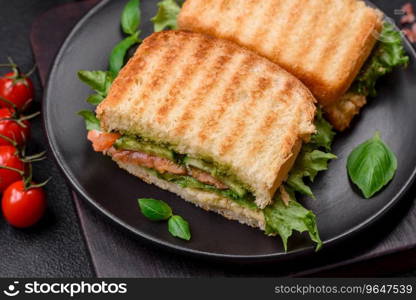 Delicious crispy sandwich with toast, salmon, avocado, tomatoes, salt, spices and herbs on a dark concrete background