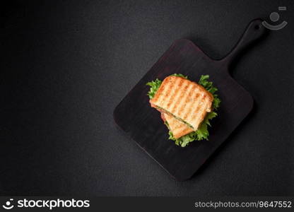 Delicious crispy sandwich with toast, salmon, avocado, tomatoes, salt, spices and herbs on a dark concrete background