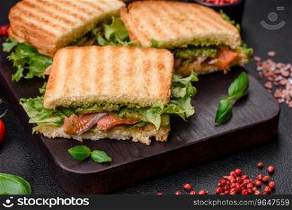 Delicious crispy sandwich with toast, salmon, avocado, tomatoes, salt, spices and herbs on a dark concrete background