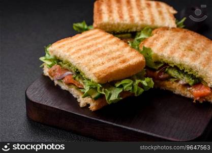 Delicious crispy sandwich with toast, salmon, avocado, tomatoes, salt, spices and herbs on a dark concrete background