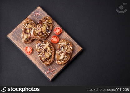 Delicious crispy toast or bruschetta with fried onion, ch&ignon mushrooms and cheese with spices and herbs on a dark concrete background