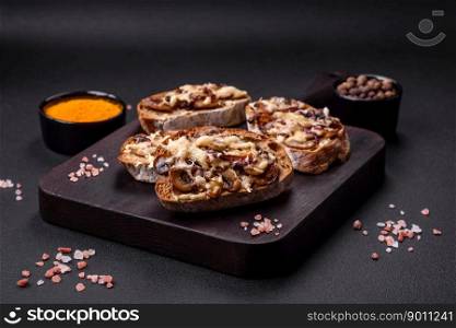 Delicious crispy toast or bruschetta with fried onion, ch&ignon mushrooms and cheese with spices and herbs on a dark concrete background