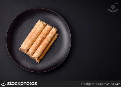 Delicious crispy wafer rolls with cream filling with nuts on a dark concrete background