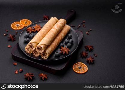 Delicious crispy wafer rolls with cream filling with nuts on a dark concrete background