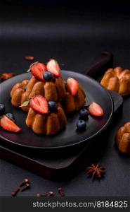Delicious cupcakes or muffins with raisins and nuts, strawberries and blueberries on a ceramic plate on a textured concrete table